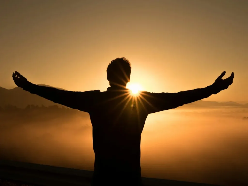 Person standing with arms outstretched at sunrise